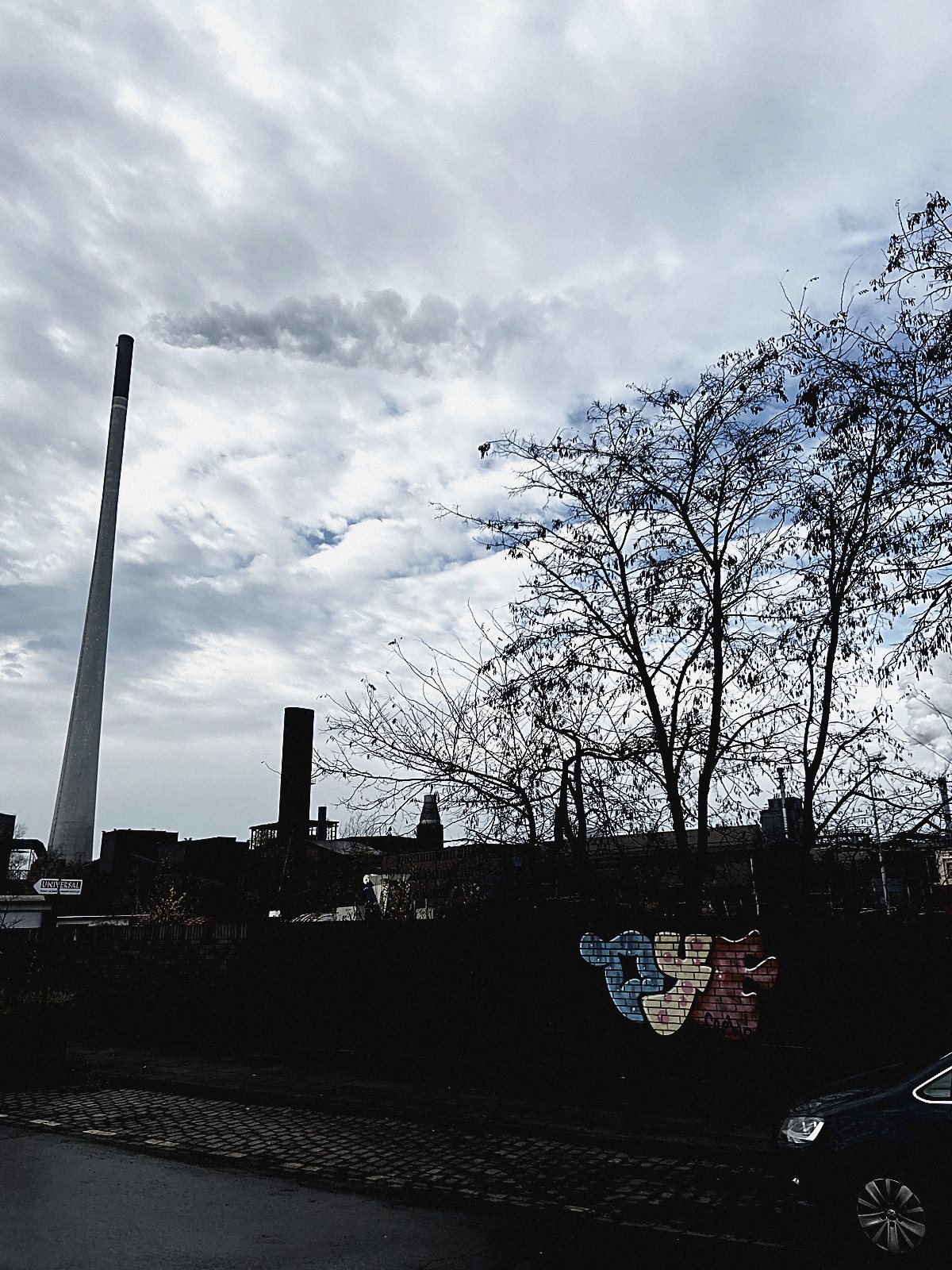 Getaggte Mauer vor Industriekulisse mit Stahlwerk und dramatischem Himmel