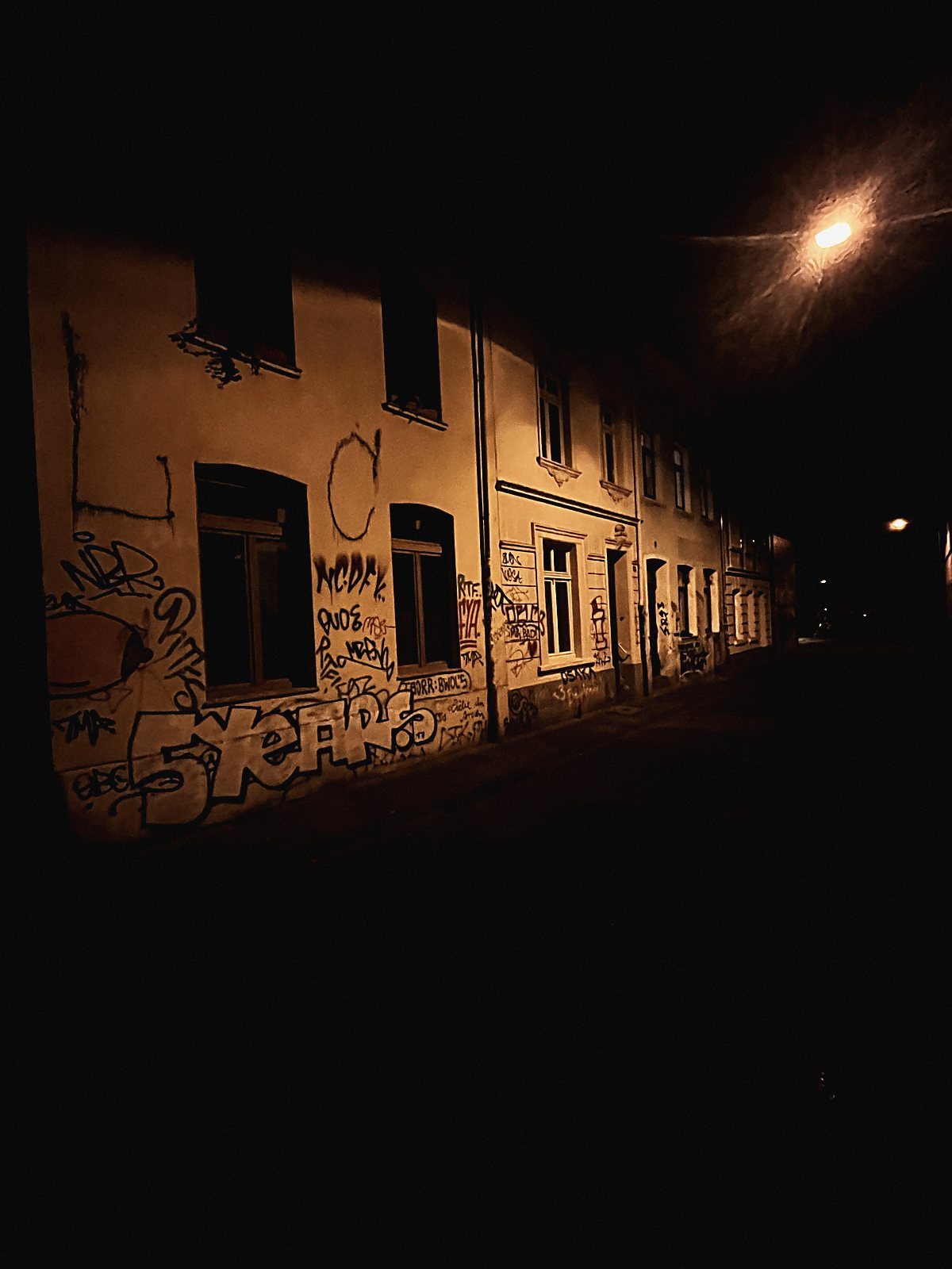 Nächtliche Straße unter Natriumlicht mit getaggter Fassade